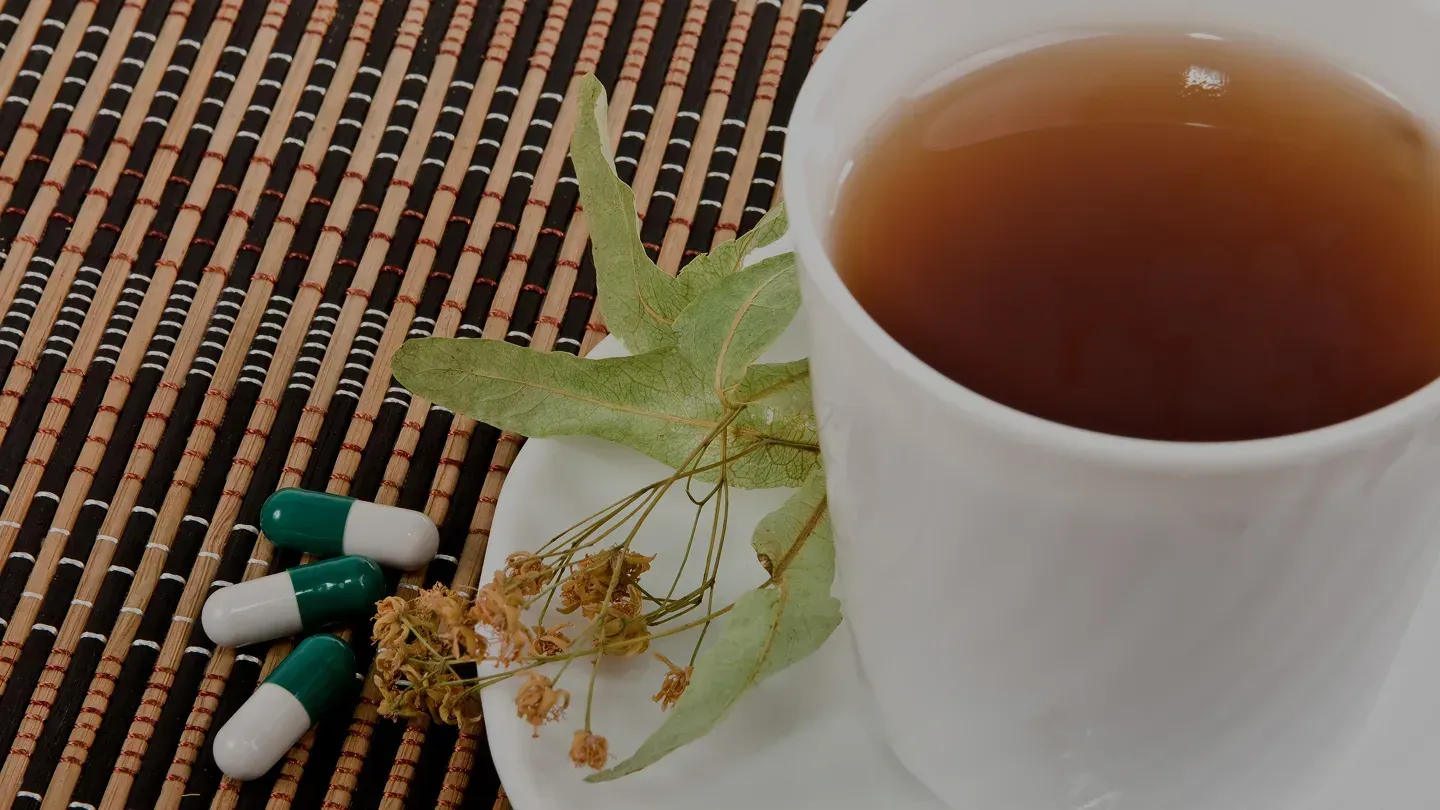 A cup of herbal tea beside linden blossoms